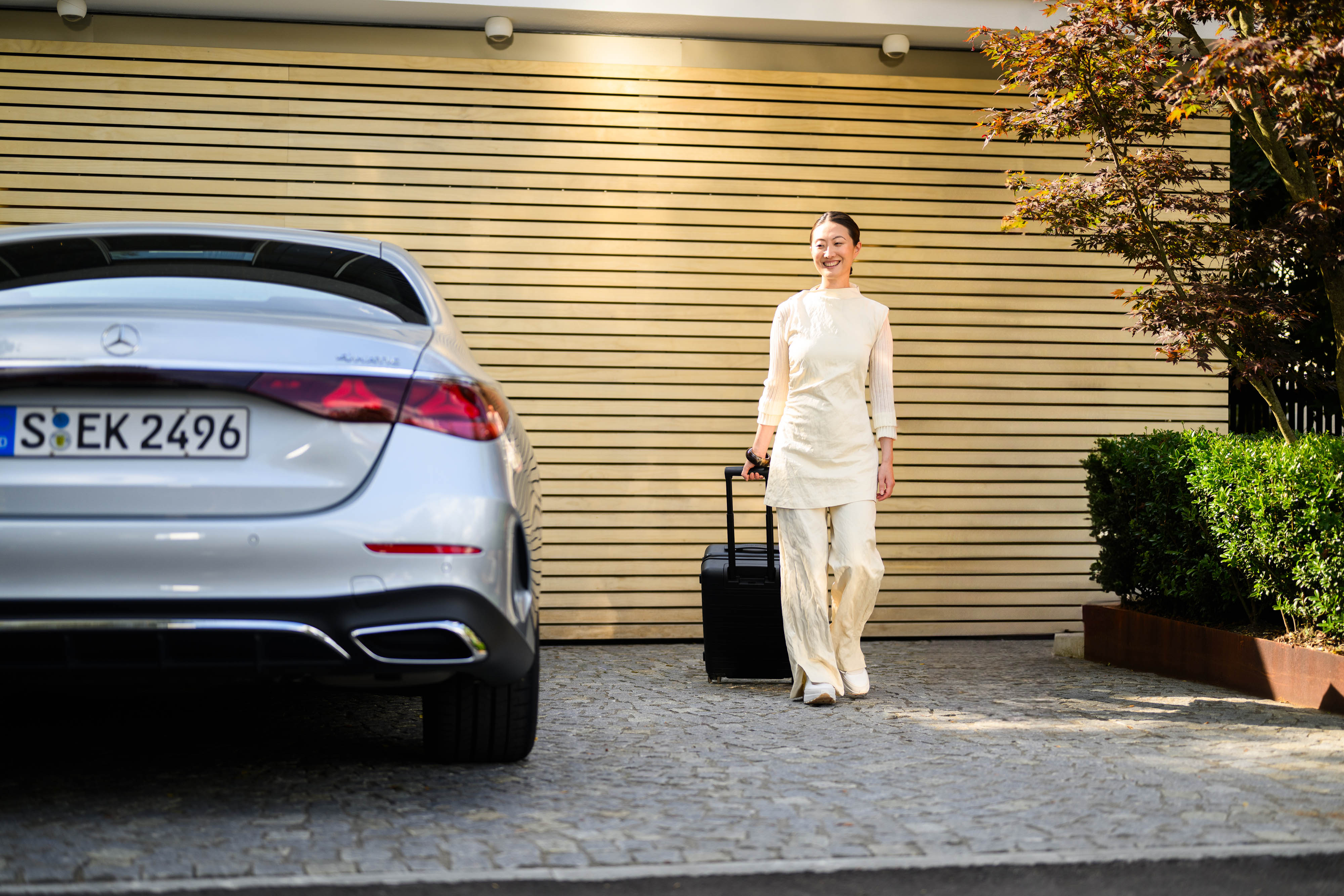 Mercedes-Benz Rent Eine Person mit Rollkoffer läuft neben einem Mercedes-Benz Fahrzeug.