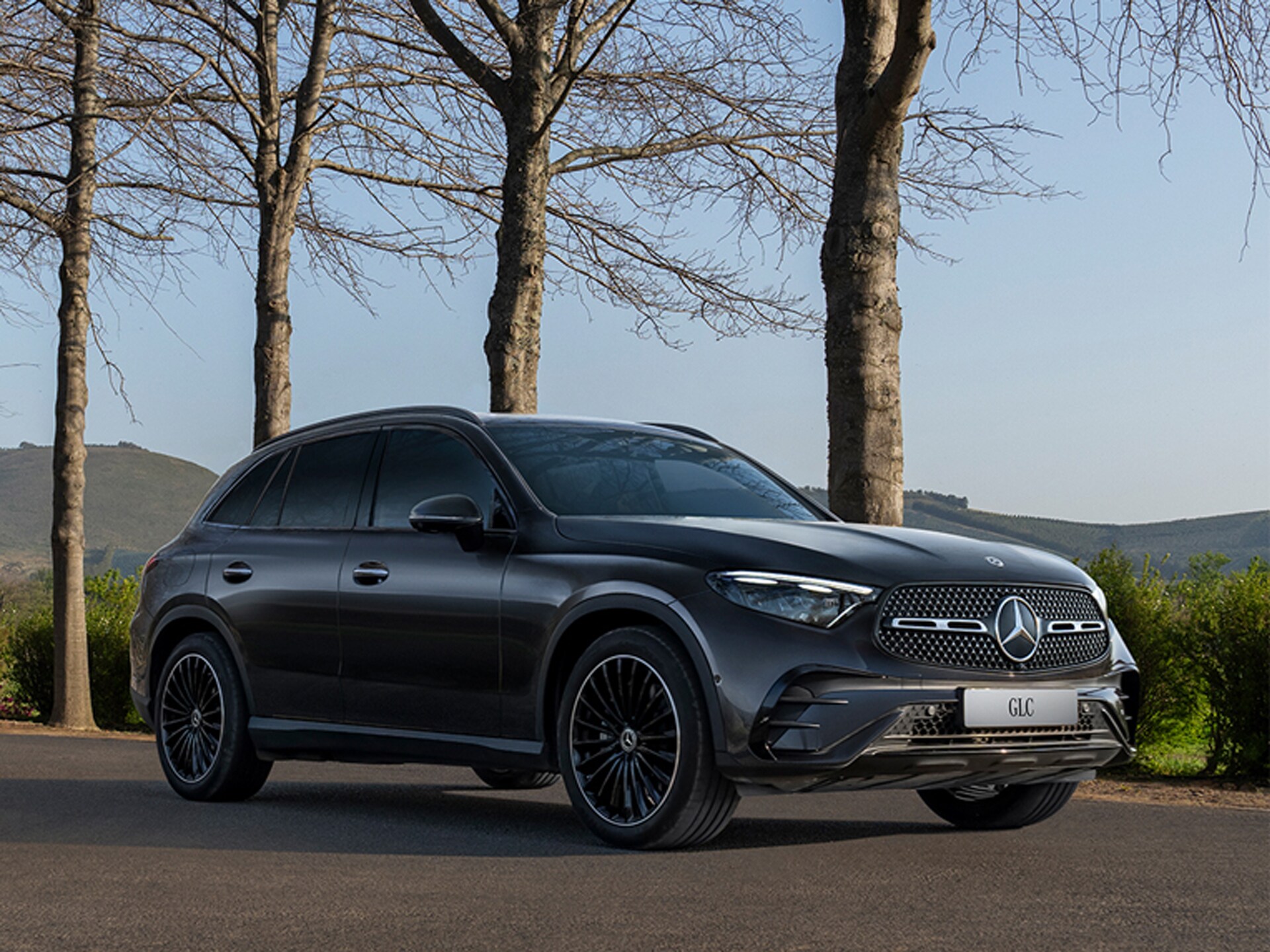 Fahrzeug-Angebote | Mercedes-Benz. Ein schwarzer Mercedes-Benz GLC SUV fährt über eine Landstrasse mit Bergen im Hintergrund.