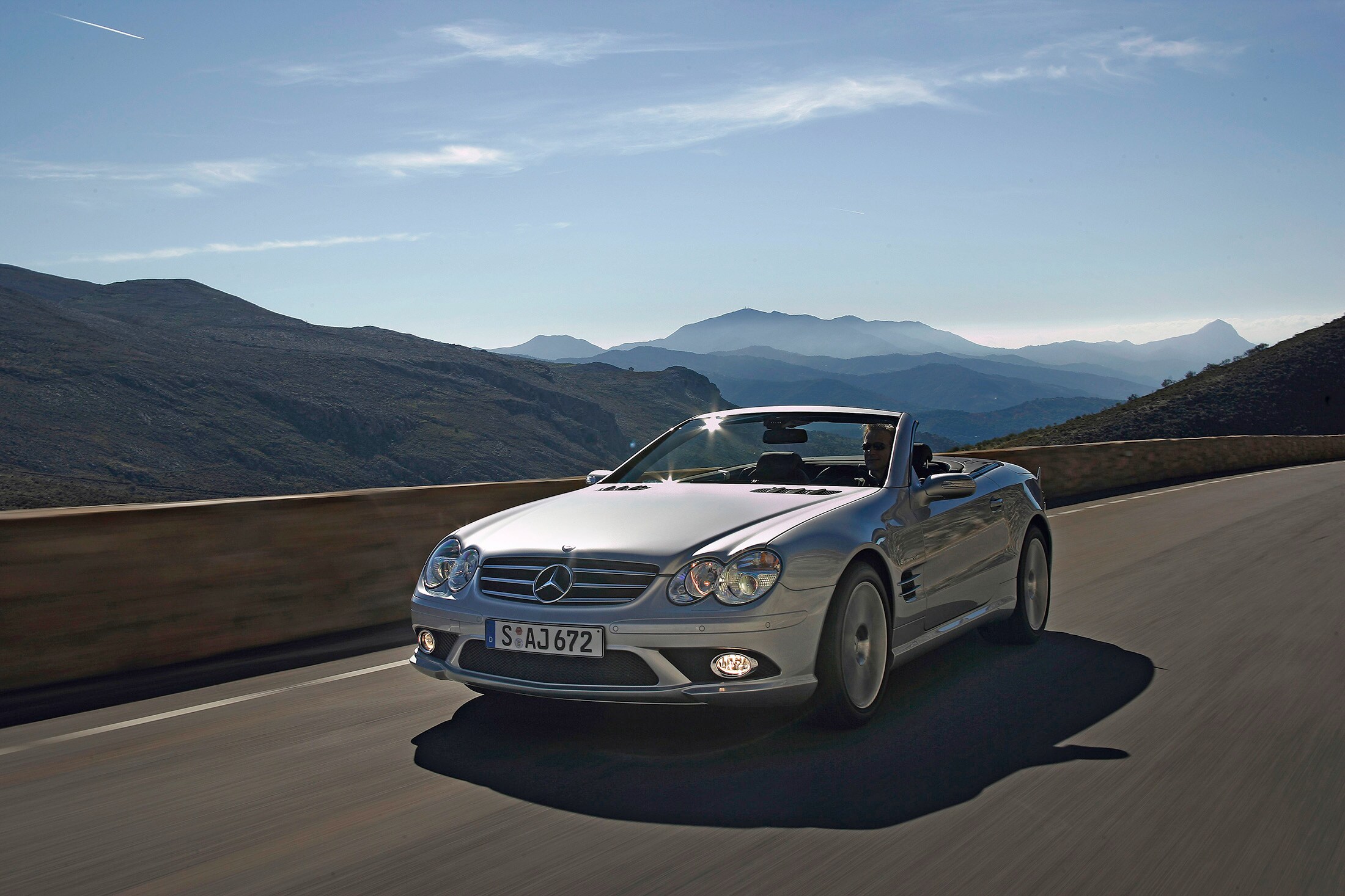 Service- und Garantiepakete | Mercedes-Benz. Ein silbernes Cabriolet von Mercedes-Benz fährt eine Straße mit Bergen entlang.