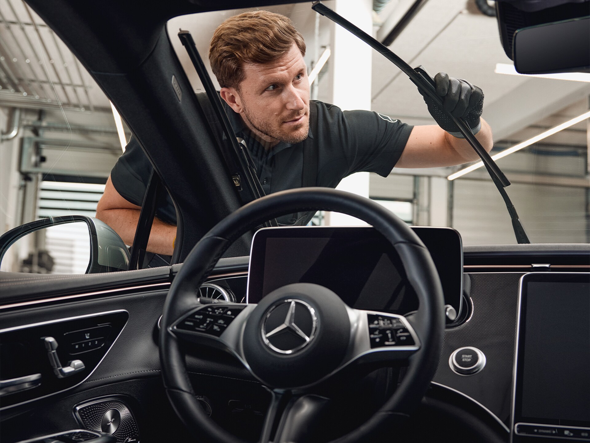 Winteraktion | Mercedes-Benz Ein Mercedes-Benz Mechaniker in Arbeitskleidung und Handschuhen beim Ersetzen der Wischblätter.