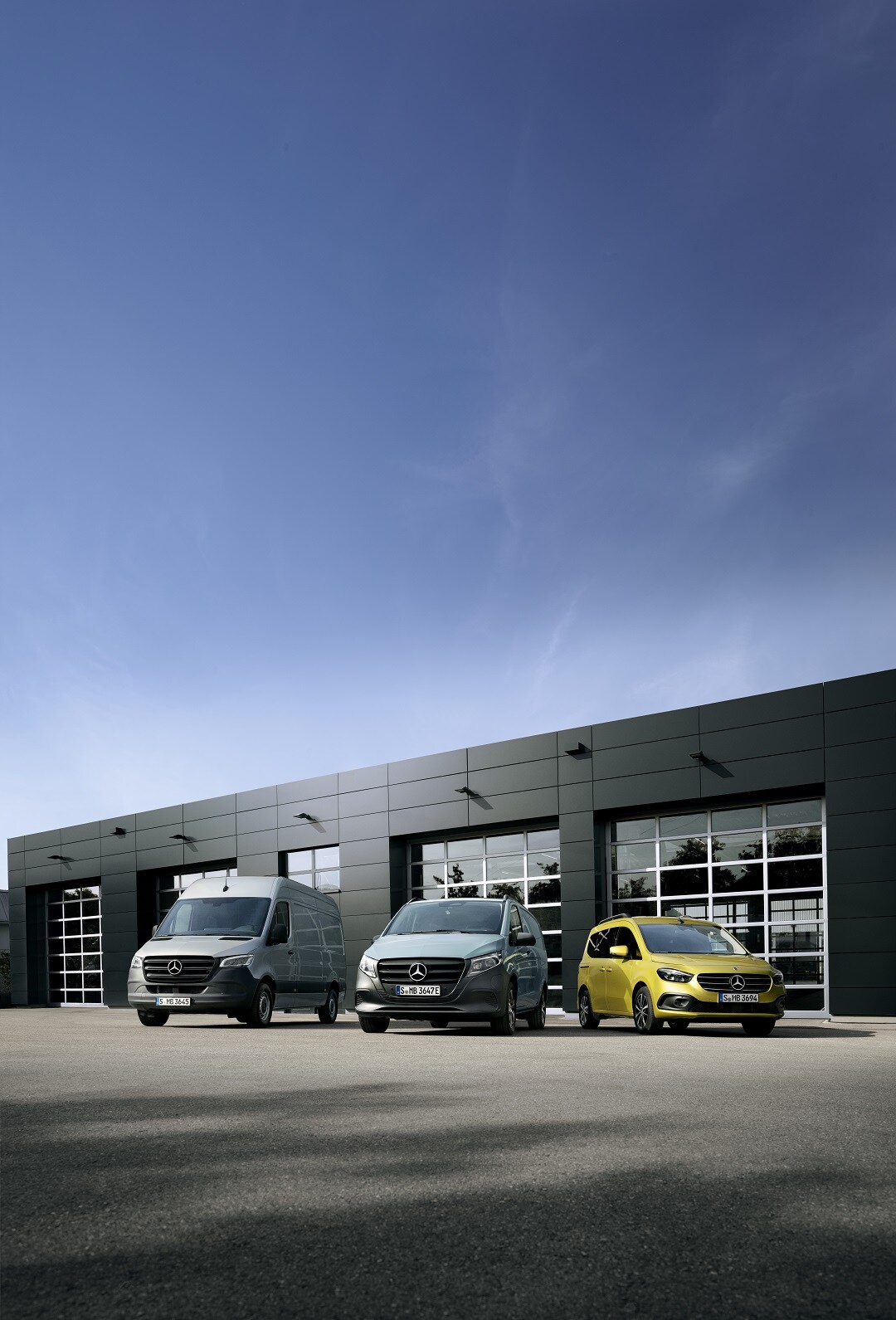 Mehrere Mercedes-Benz Transporter in einer Reihe vor modernem Gebäude, aufgenommen bei Tageslicht.