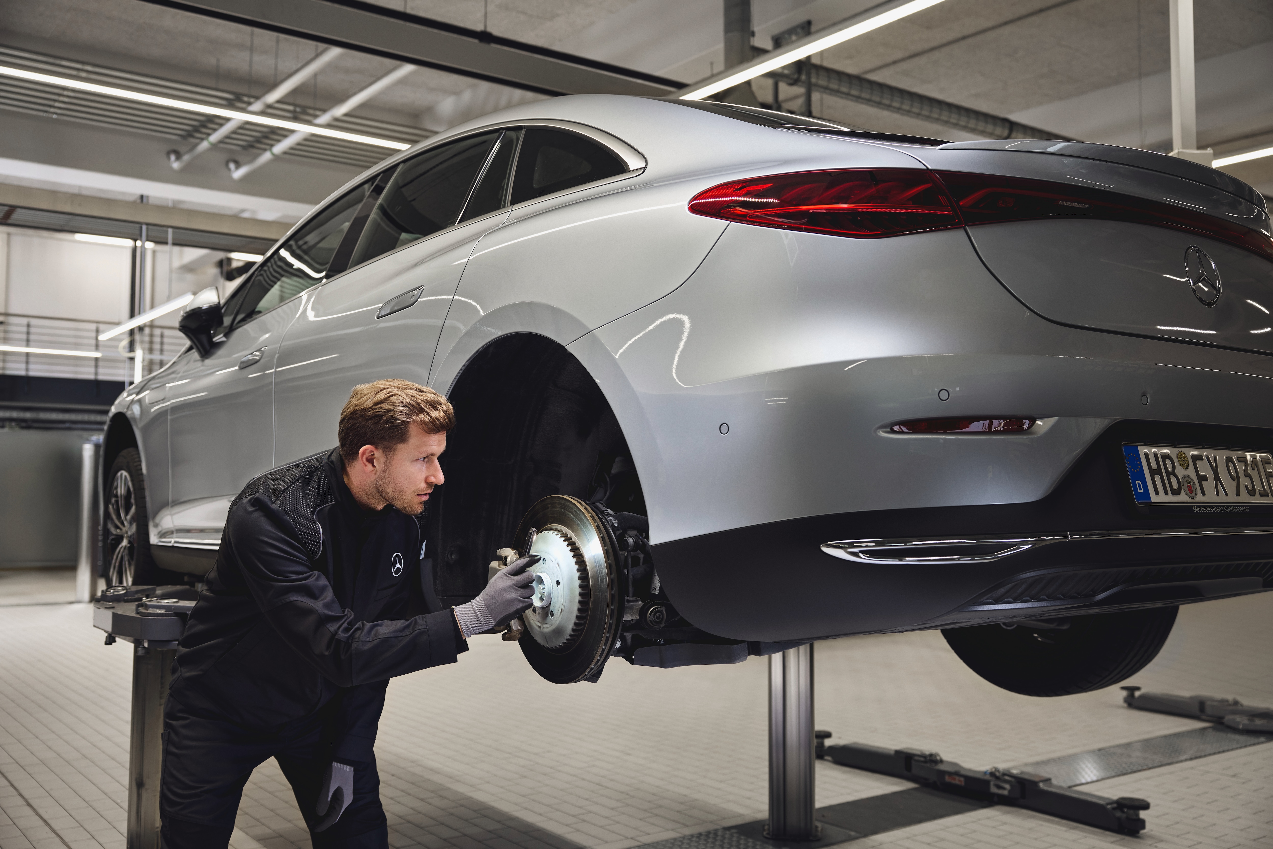 Ersatzteile | Mercedes-Benz Ein Mercedes-Benz-Fahrzeug steht auf einer Hebebühne, während ein Techniker die hintere Bremsanlage im Rahmen eines Austauschs von Originalteilen überprüft.