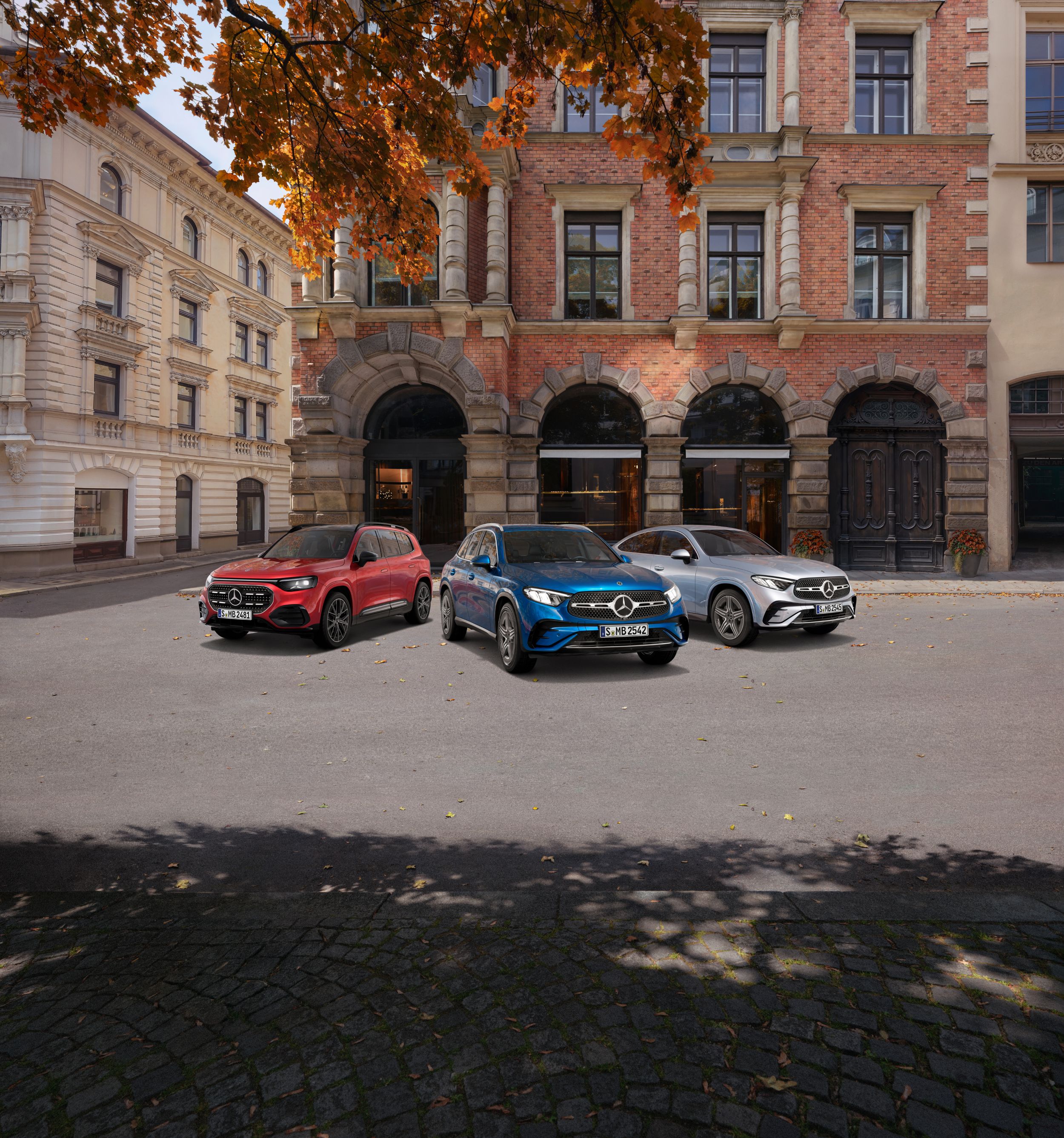 3 Mercedes-Benz Modelle in Rot, Blau und Silber stehen nebeneinander auf einer Straße in einer urbanen Umgebung. Die Sonne scheint.
