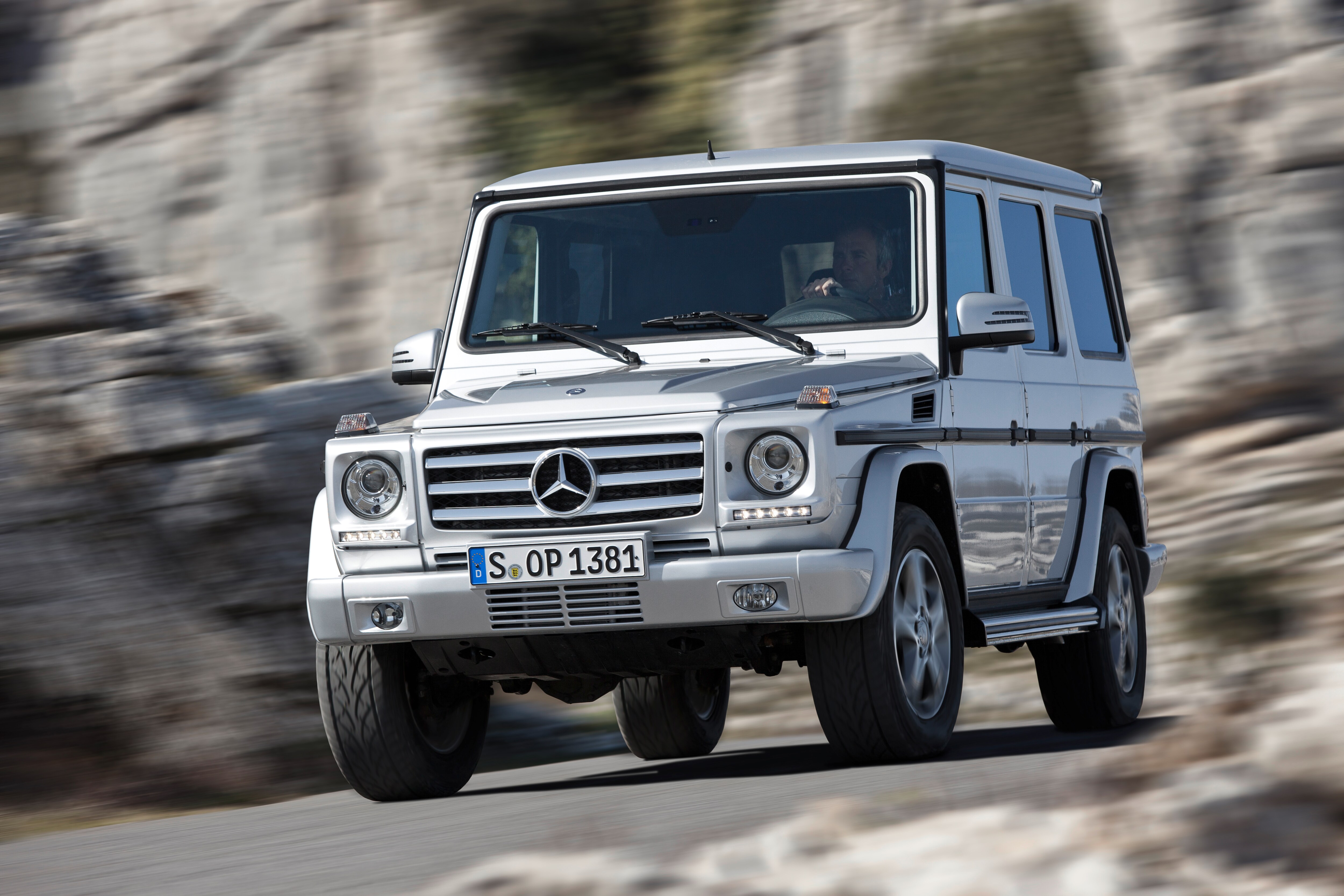 Service- und Garantiepakete | Mercedes-Benz. Eine silberne G-Klasse von Mercedes-Benz in Bewegung vor einer steinernen Felswand.