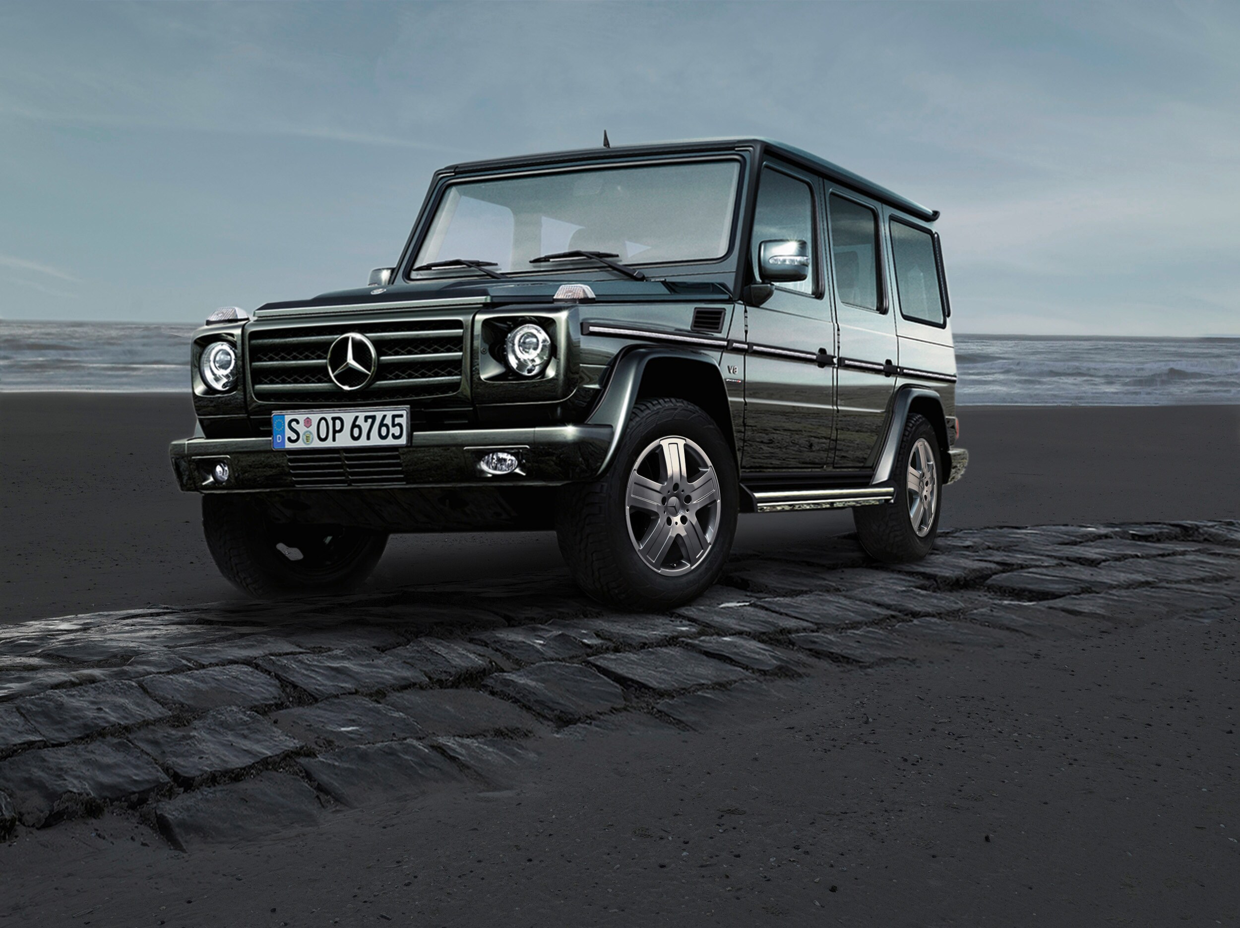 Service- und Garantiepakete | Mercedes-Benz. Eine dunkle G-Klasse von Mercedes-Benz steht auf einem gepflasterten Streifen vor der Küste.