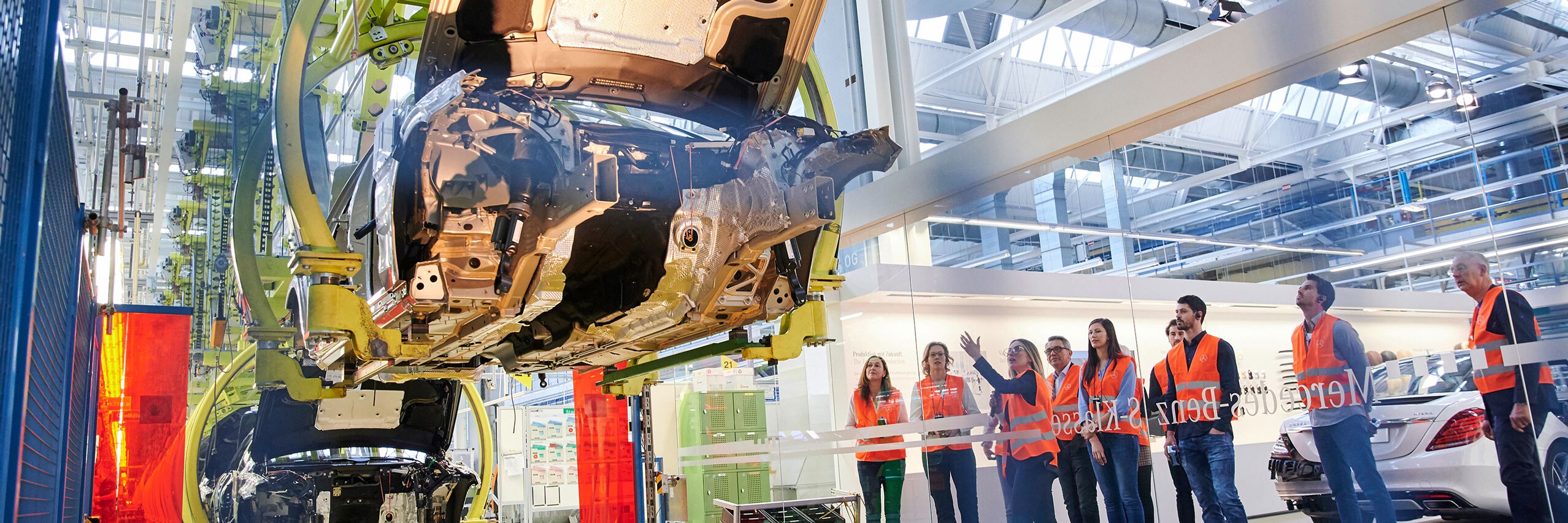 Eine Gruppe von Menschen schaut sich in einer Werkbesichtigung im Kundencenter an, wie ein Mercedes-Benz zusammengebaut wird.