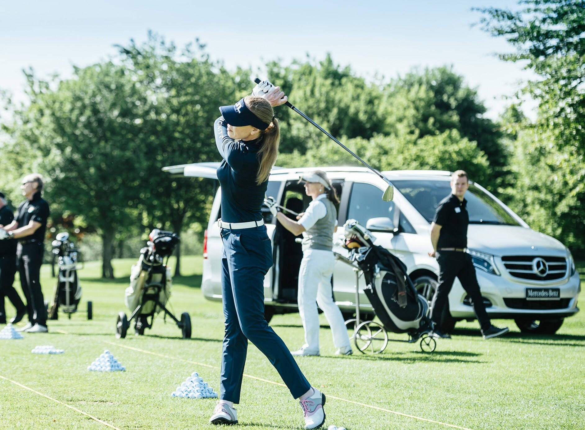 Golf | Mercedes-Benz Ein Golfspielerin schlägt einen Ball übers Feld. Eine Menschenmenge schaut dabei zu.