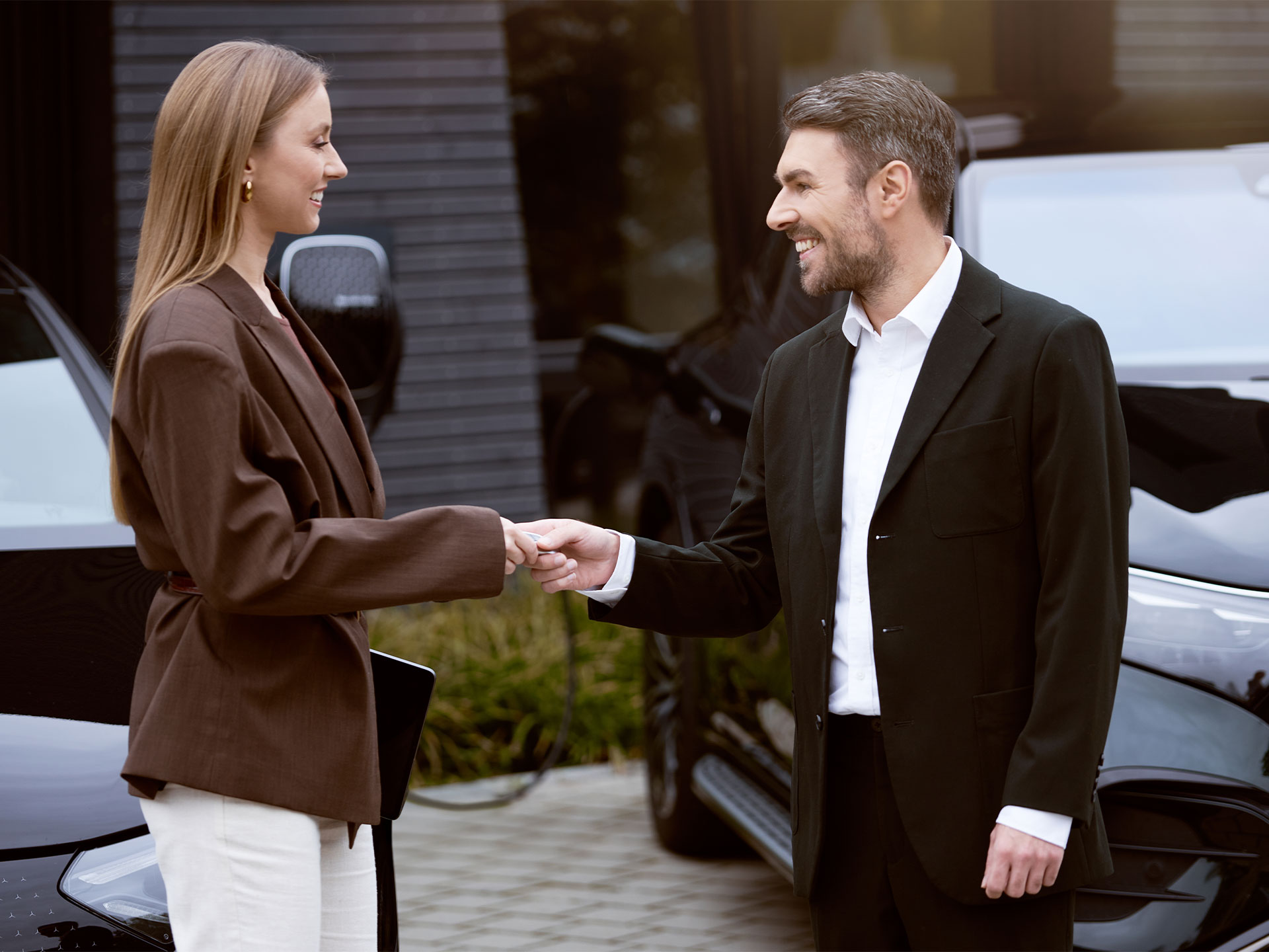 Laden für Geschäftskunden | Laden | Mercedes-Benz Zwei Personen schütteln sich die Hand, während im Hintergrund Mercedes-Benz Fahrzeuge laden.