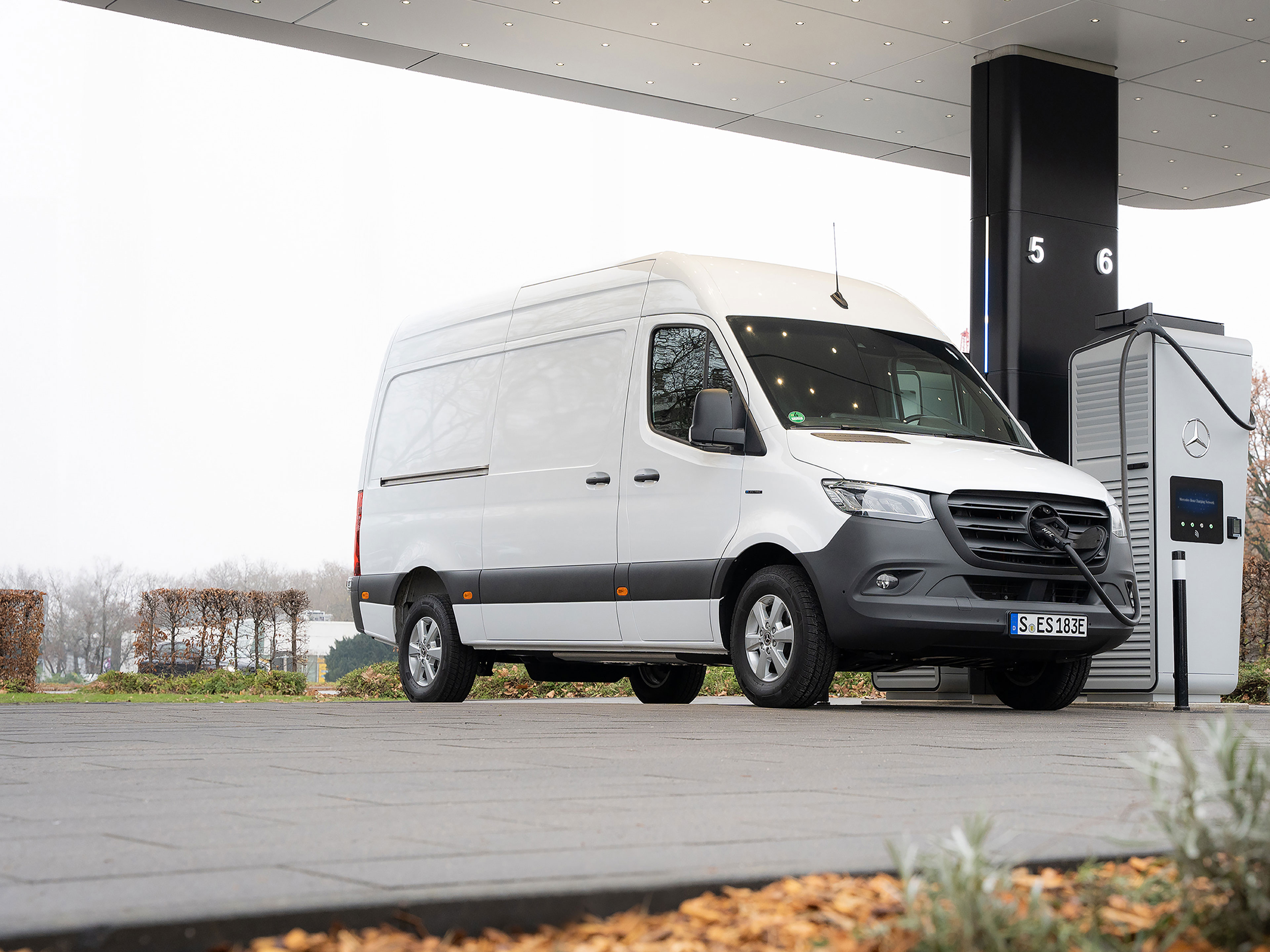 Ein weißer Sprinter Kastenwagen, wird an einer E-Ladesäule auf einem Parkplatz geladen.